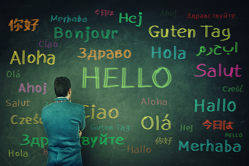 Rear view of a puzzled businessman in front of a huge chalkboard written with the word hallo in different languages and colors.